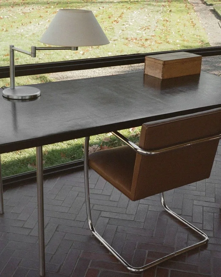 A modern desk with a lamp, wooden box, and brown leather chair.