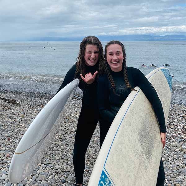 Two girls laughing while holding surfboards.