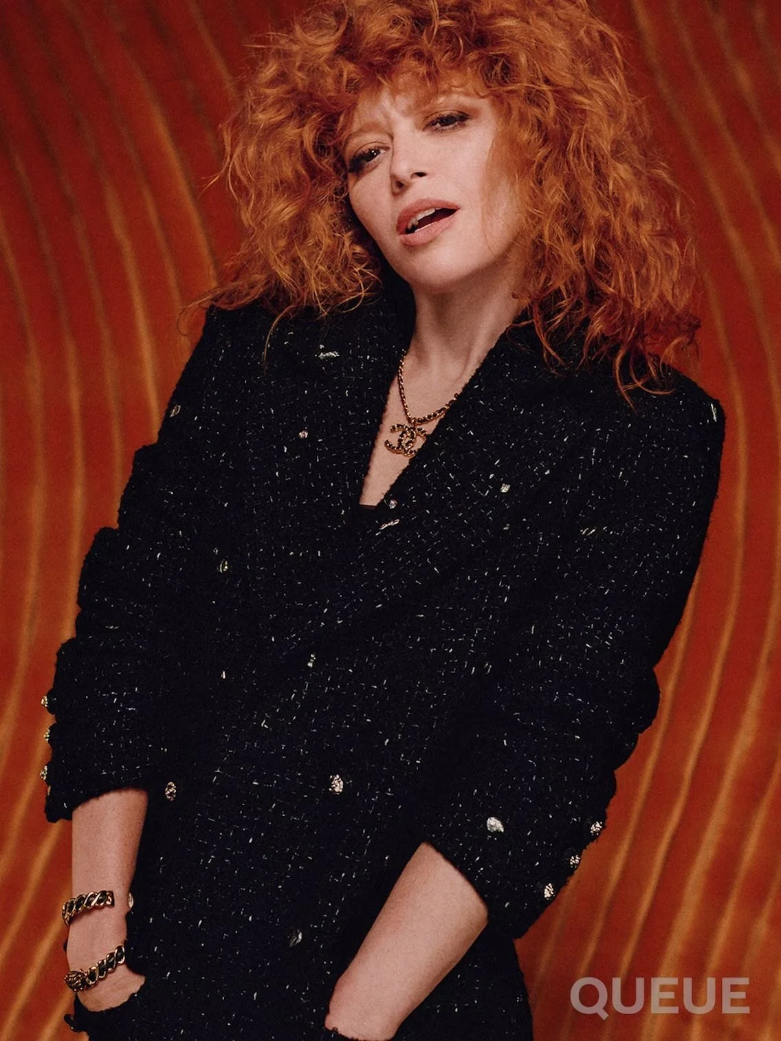 Natasha Lyonne in black tweed against an orange wave wall