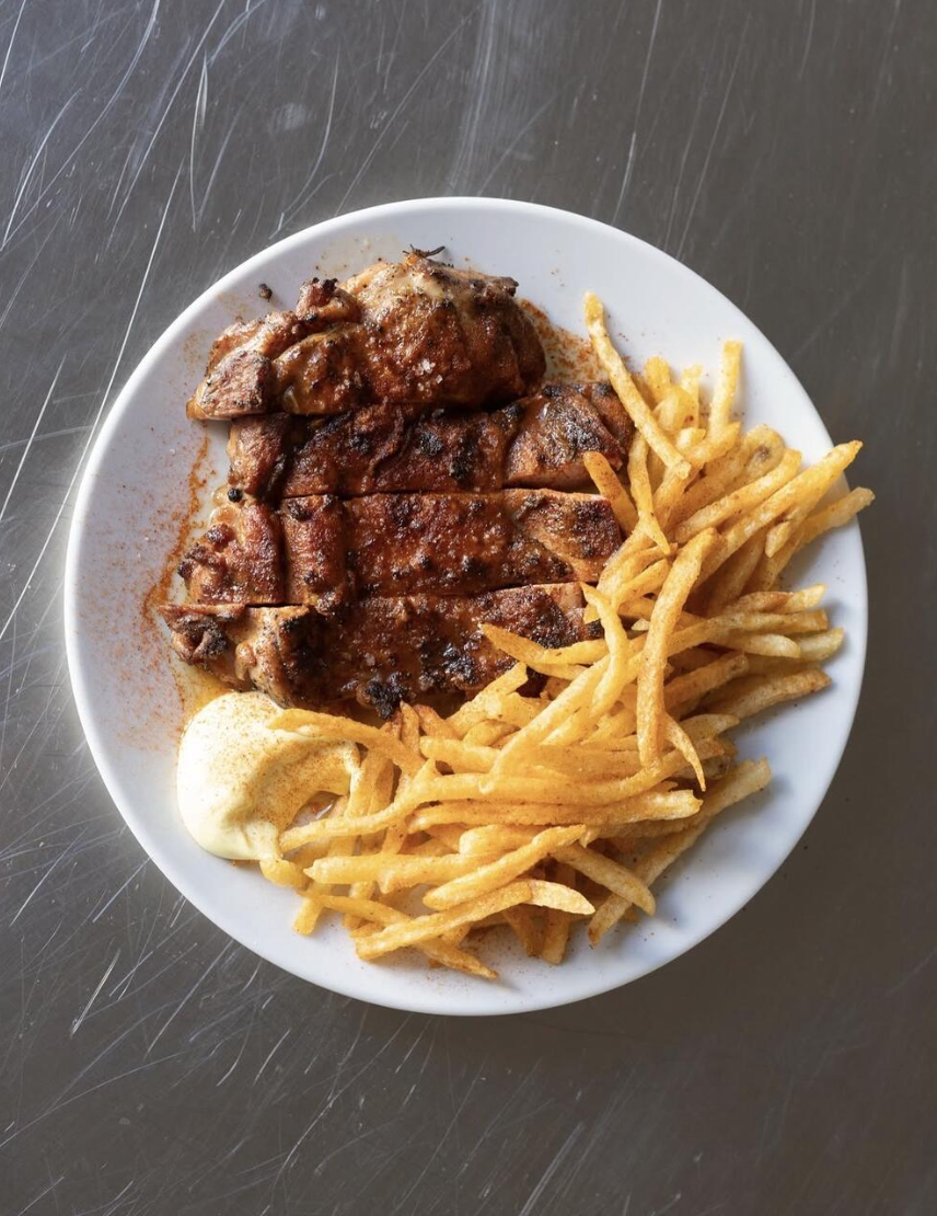 Grilled meat with thin fries and aioli on a white plate over steel