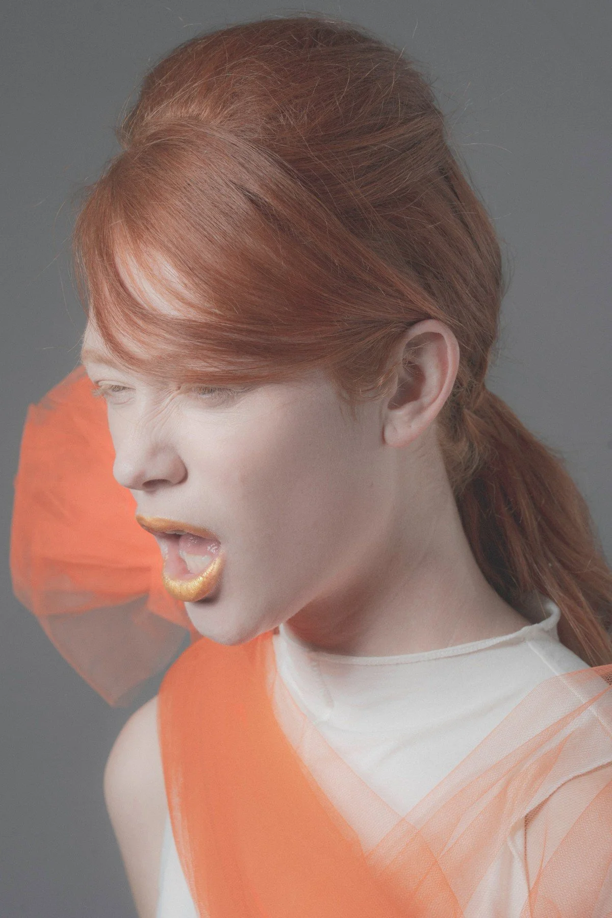 Red-haired model in profile with gold lips, orange tulle over a white top