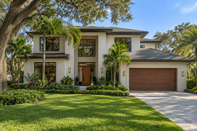 Illustrative two-story custom Florida home with warm stucco, bronze windows, a wood-accented entrance and landscaped front yard.