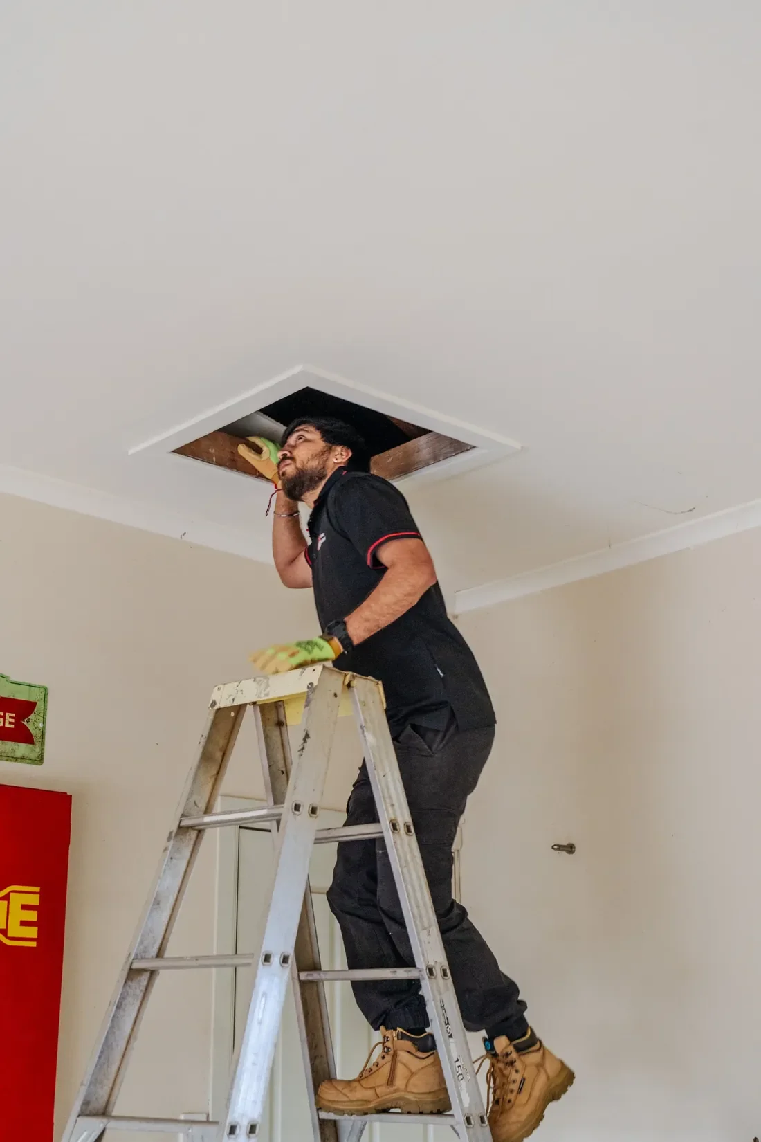 RMA engineer inspecting a ceiling access hatch from a ladder