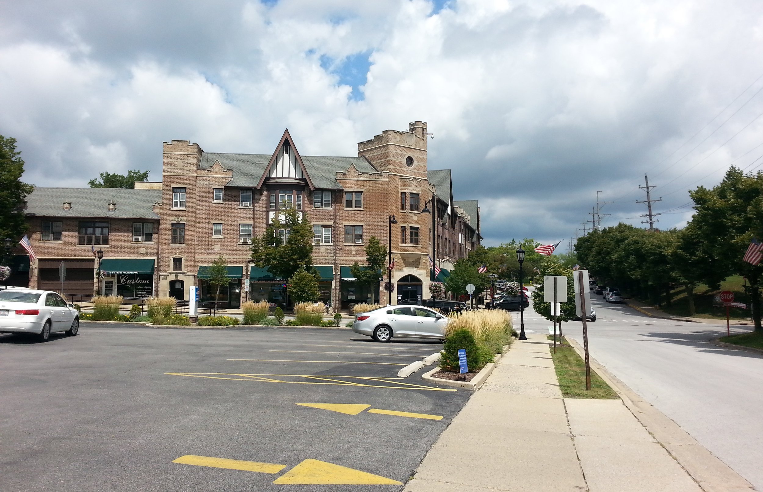 Downtown Flossmoor's Tudor Revival brick and half-timbered shop block with a clock tower, beside a tree-lined road