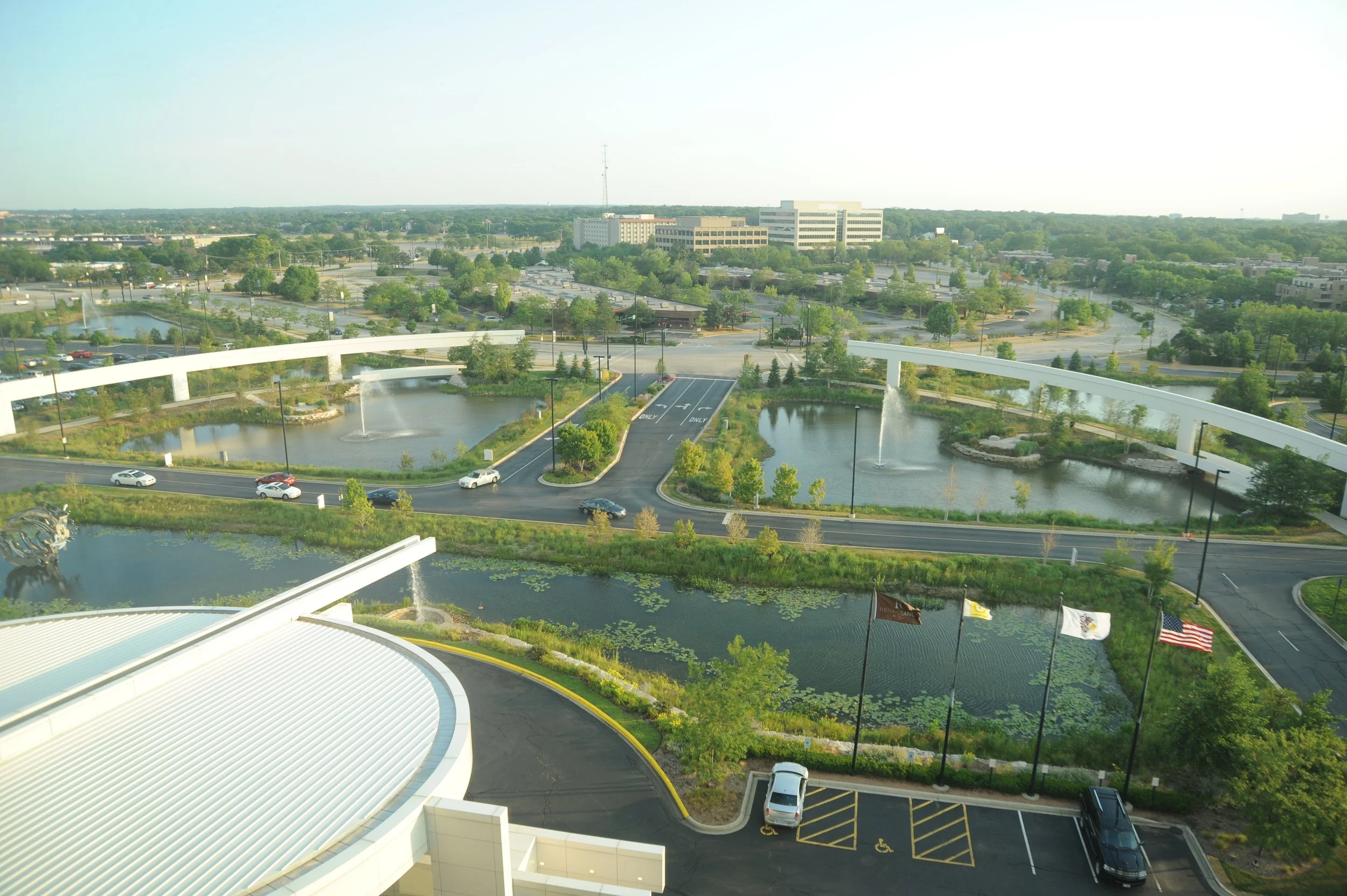 Ponds with fountains, elevated walkways, and low-rise buildings seen from above beside the Renaissance Schaumburg Hotel and Convention Center in Schaumburg