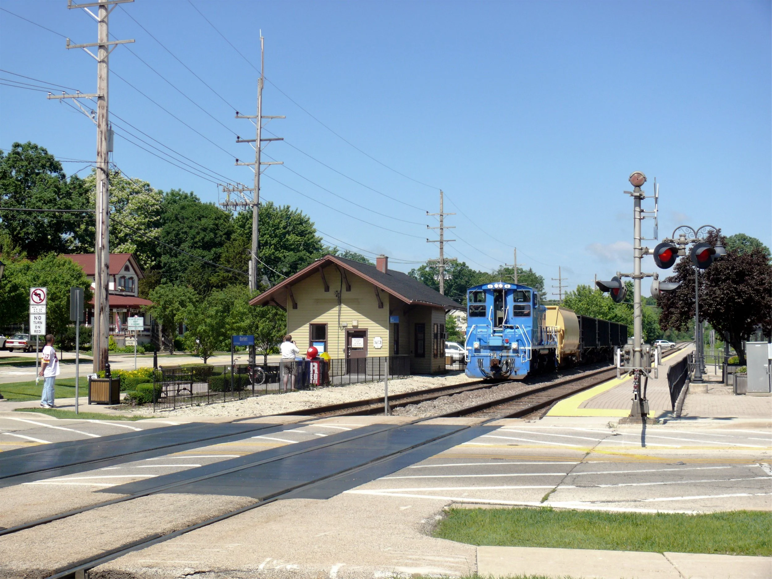 A yellow building beside the railroad tracks in Bartlett as a freight train passes, with crossing signals in front