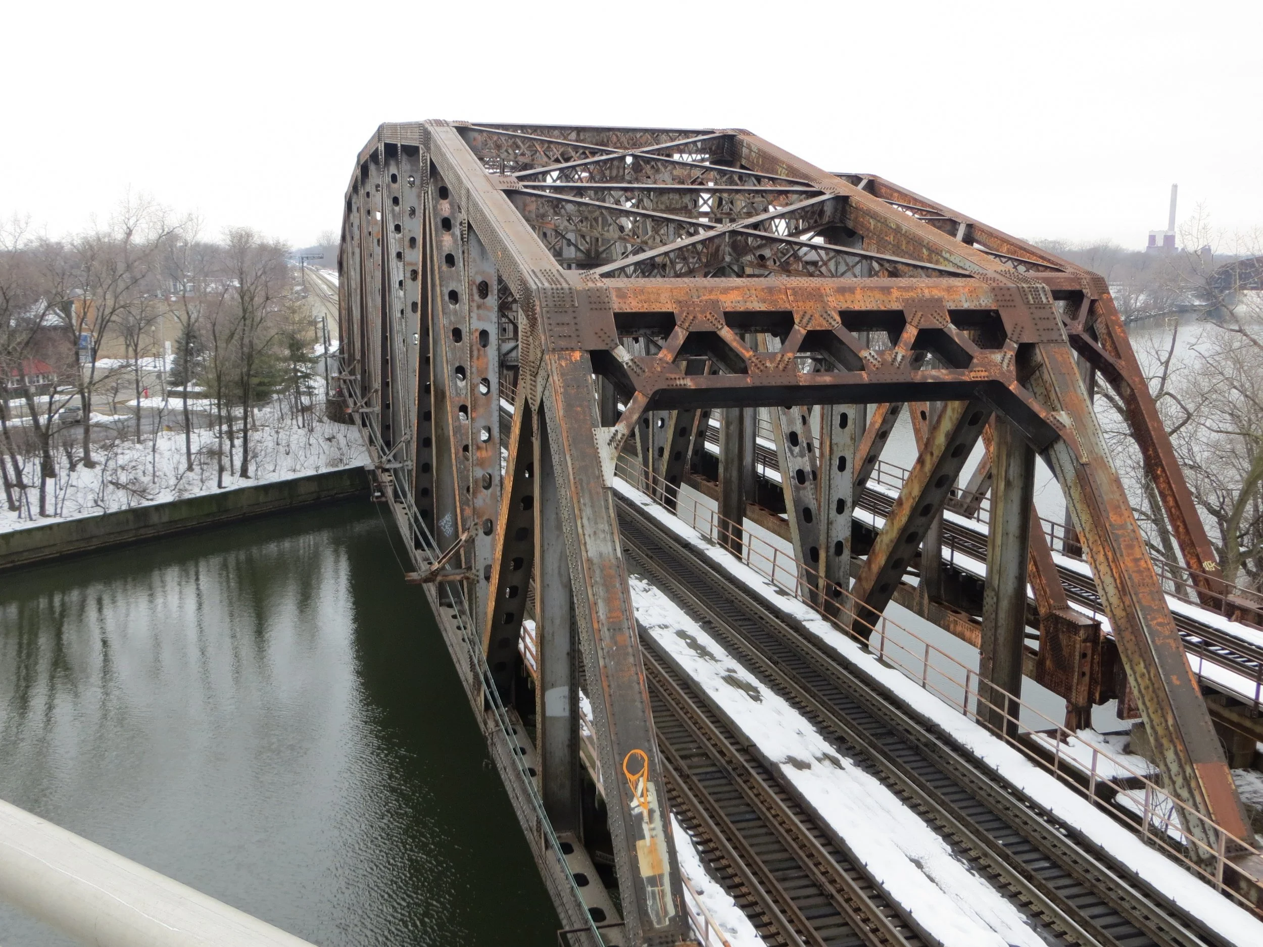 Rusted steel truss railroad bridge over a canal in Blue Island, with snow on the tracks
