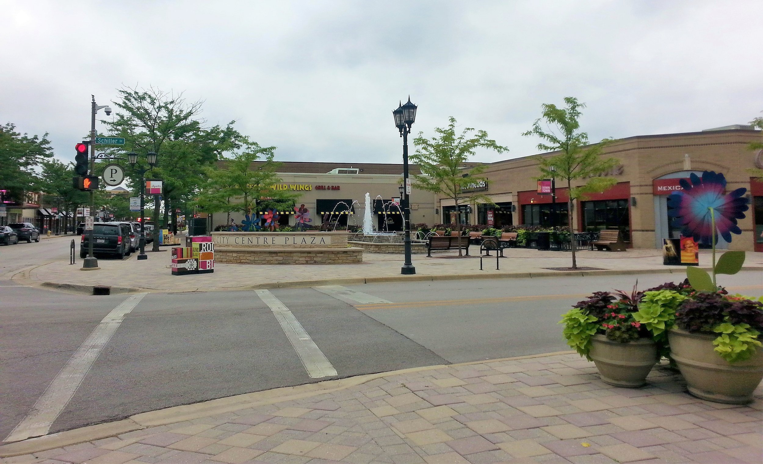 City Centre Plaza in downtown Elmhurst, with a fountain, planters, and storefronts
