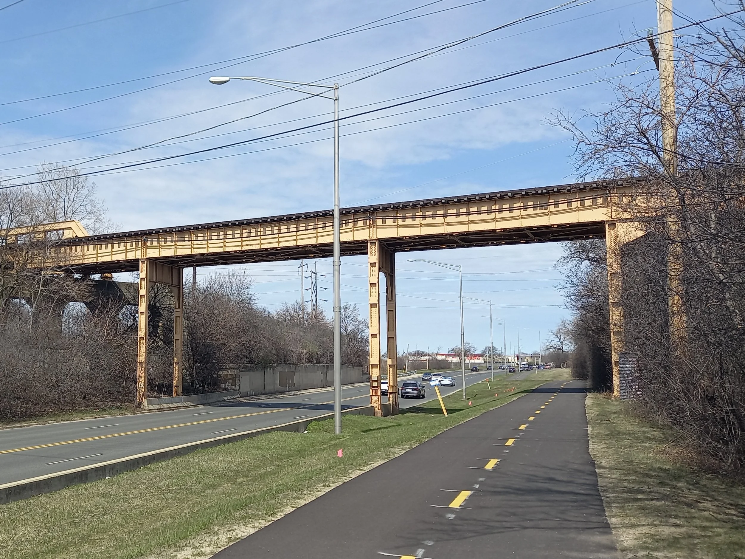 The elevated CTA Yellow Line tracks crossing McCormick Boulevard, with a paved bike path in the foreground and bare trees along the road