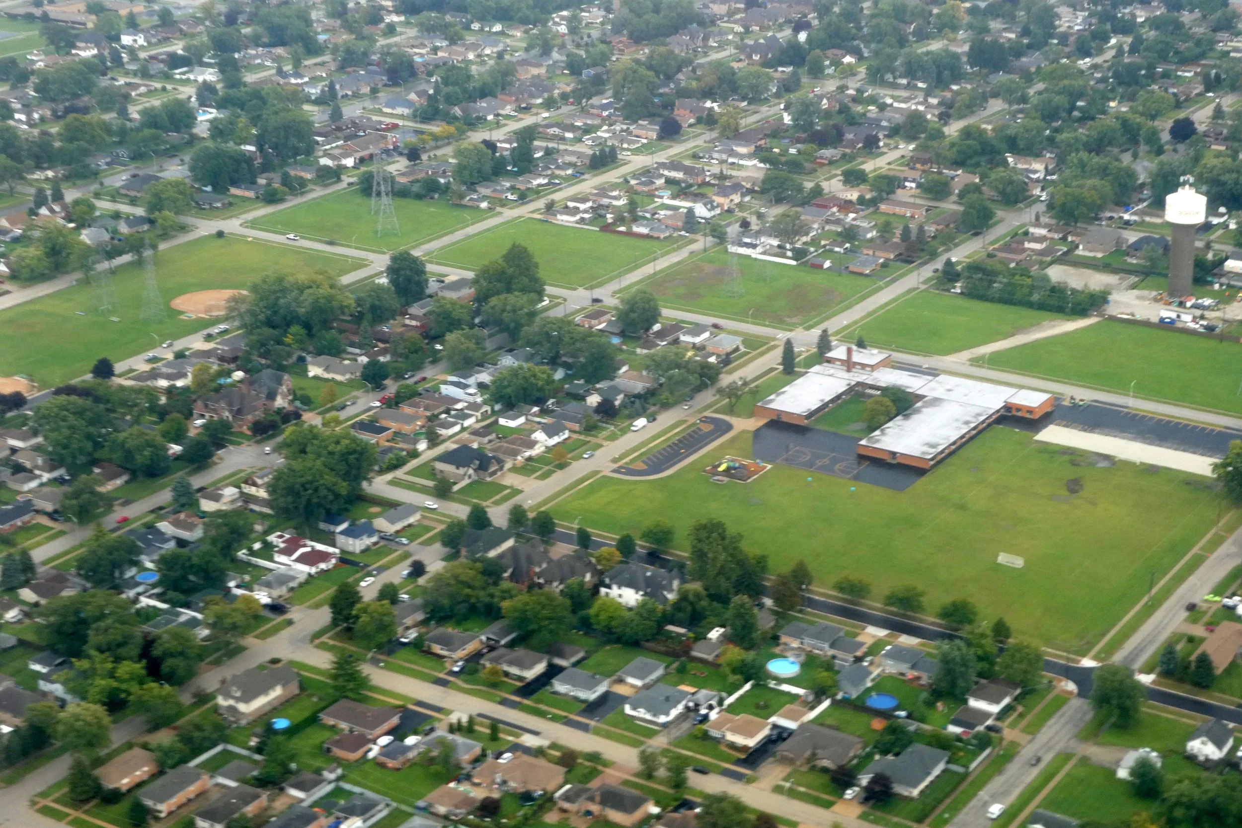 Aerial view of Bridgeview streets with ball fields, a school building, and a white water tower at right