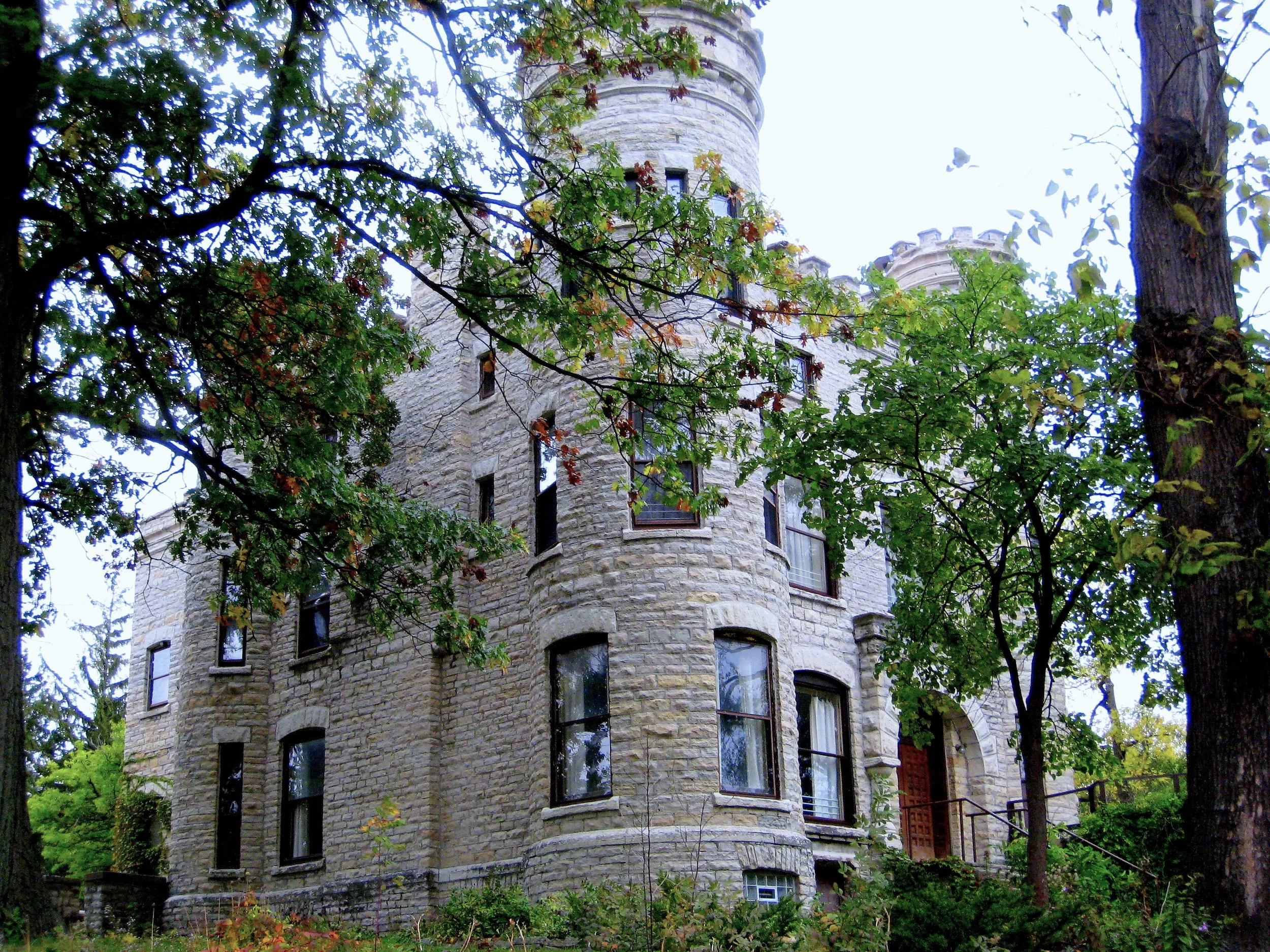 Gray limestone castle with round towers and crenellated tops seen through autumn trees