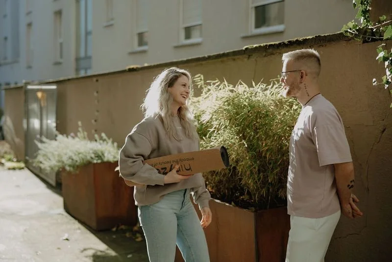 Two people laughing outdoors, one holding a hiryze yoga mat