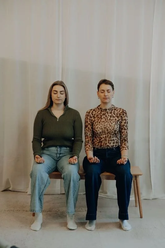 Two women sitting on a bench with eyes closed, breathing