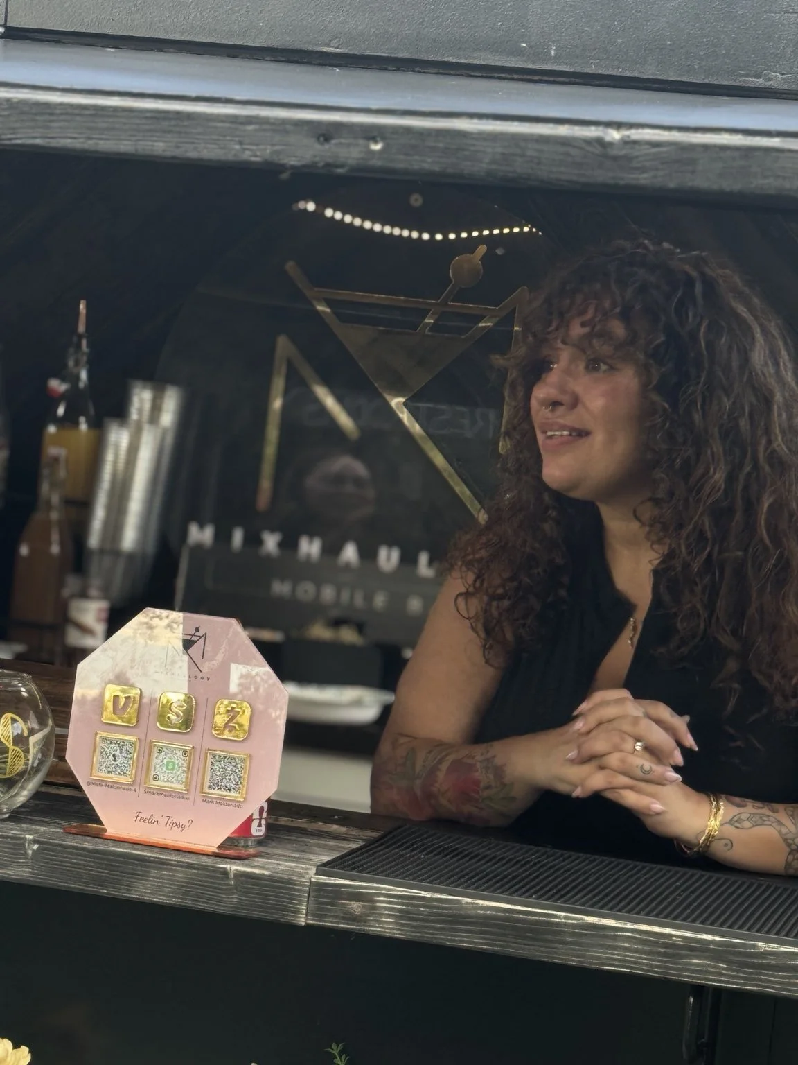 A smiling Mixhaulogy bartender serving guests from the vintage trailer