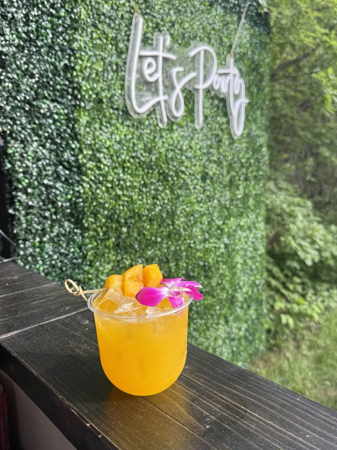 Floral-garnished golden cocktail against the Mixhaulogy greenery backdrop