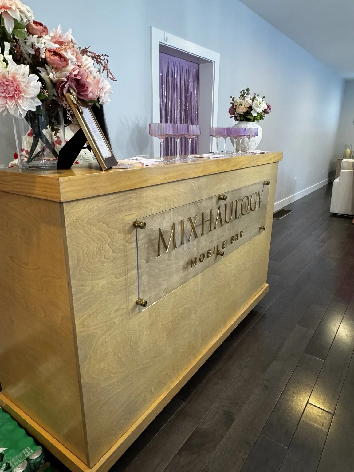 Mixhaulogy portable wooden bar styled with flowers and pink cocktail glasses indoors