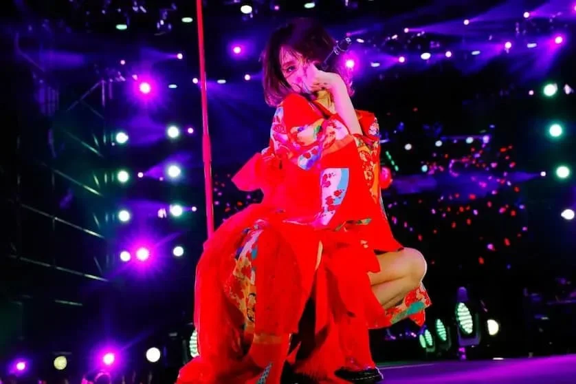LiSA performing on stage in a red outfit under purple lights