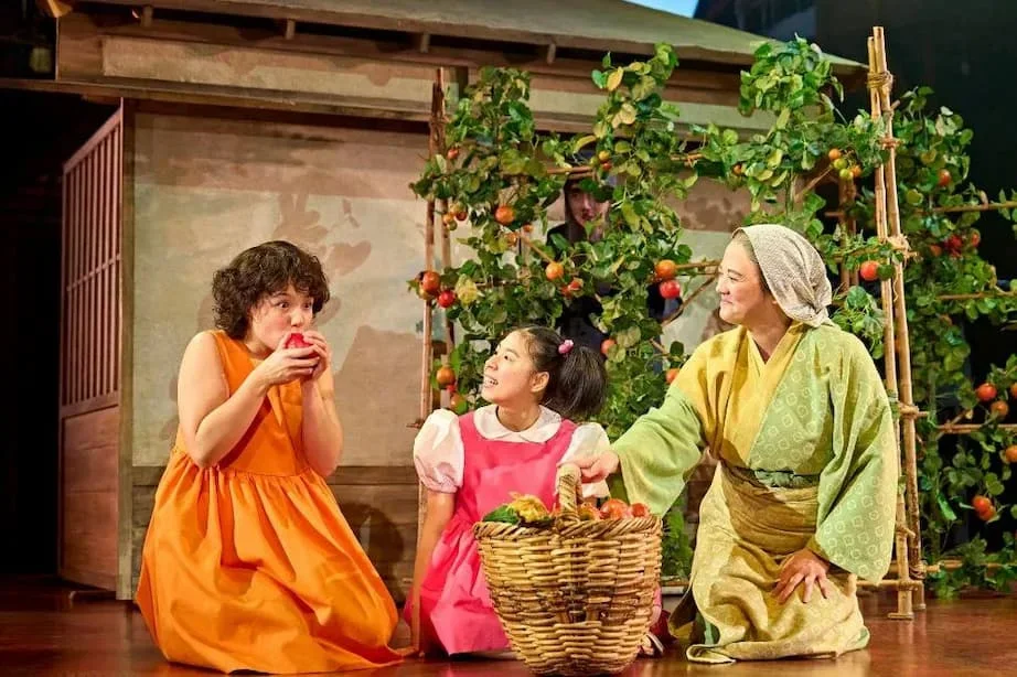 Three performers in My Neighbour Totoro sharing food beside a basket of vegetables