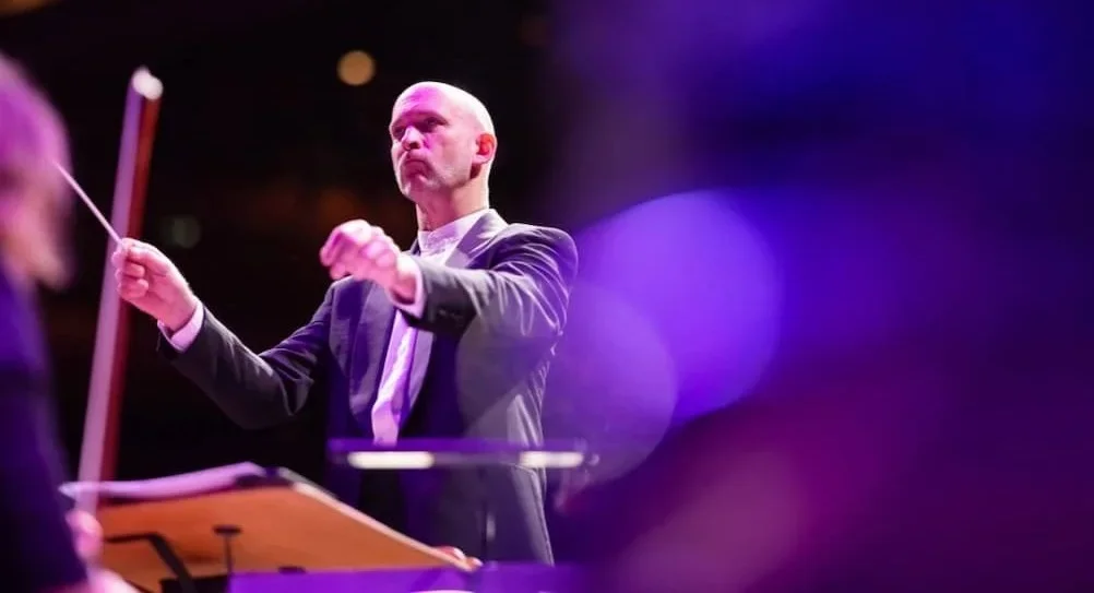 Conductor Michael England leading an orchestra under purple light