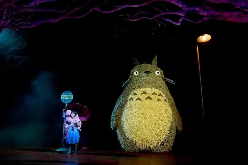 Totoro beside a girl at a bus stop on a dark stage
