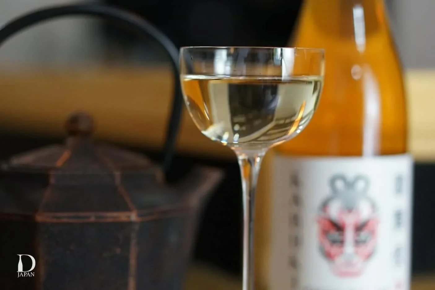 A glass of sake beside a bottle and a cast iron teapot