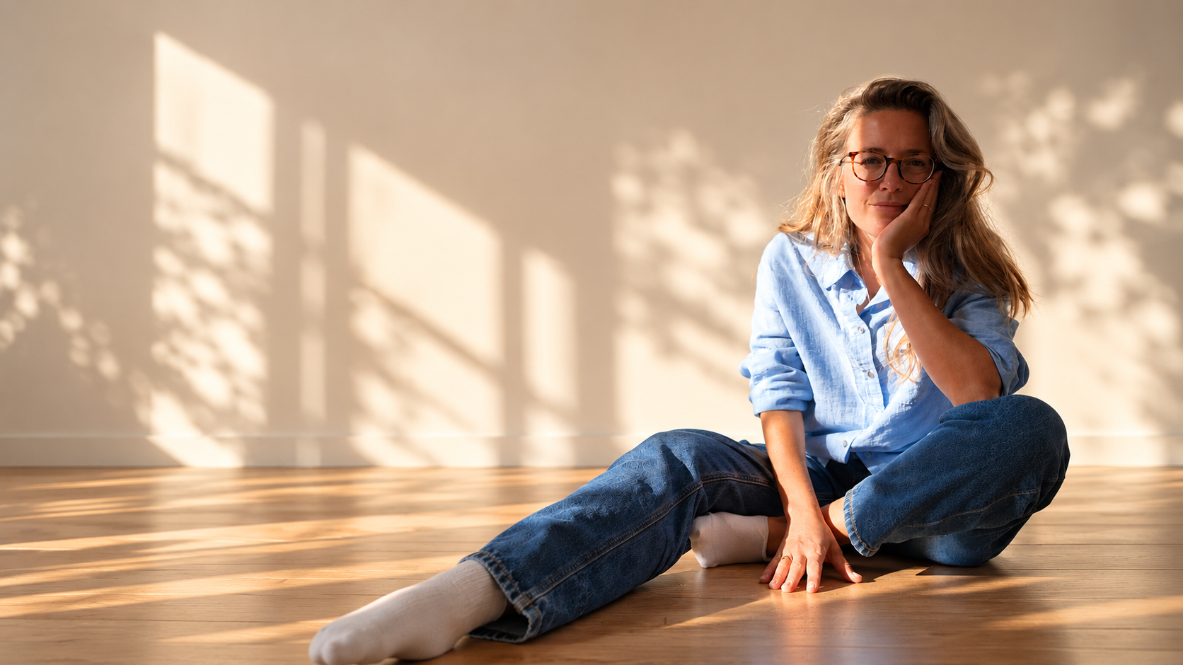 Fieke in een blauwe blouse, zittend bij het raam met bladerschaduwen op de muur