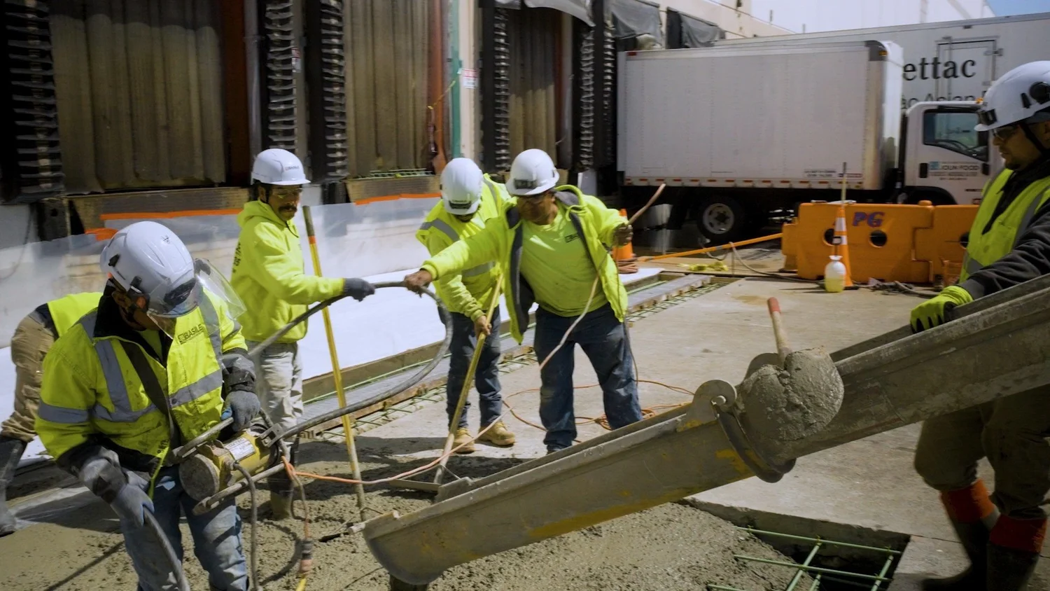 Concrete crew guiding a pump hose across a slab with a delivery truck behind