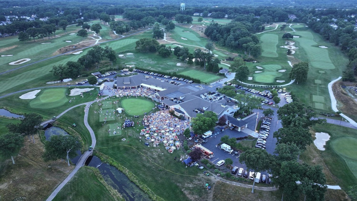 Wide drone aerial of a clubhouse, golf course and surrounding neighborhood at a country club