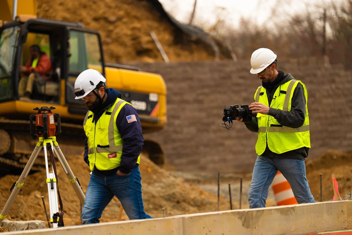 Videographer in hi-vis filming a surveyor at work on an excavation site