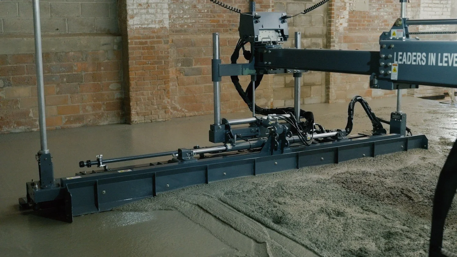 Construction marketing video still of a laser screed leveling fresh concrete inside a warehouse