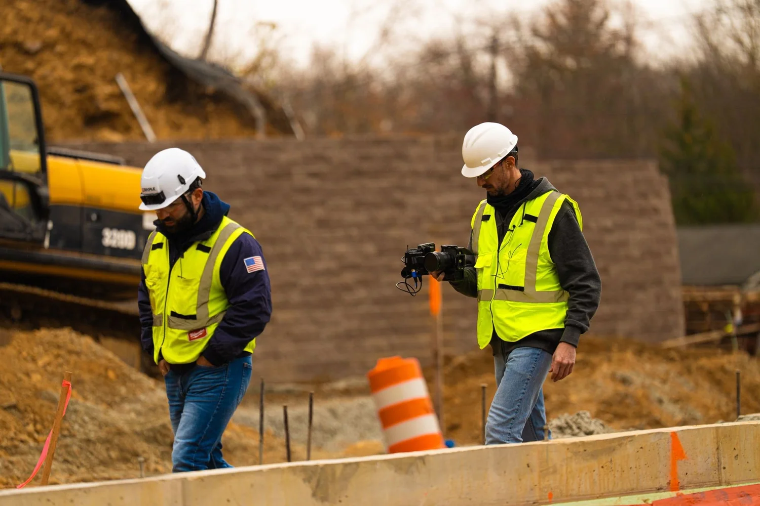 Videographer with a gimbal filming beside a surveyor and tripod on an excavation site