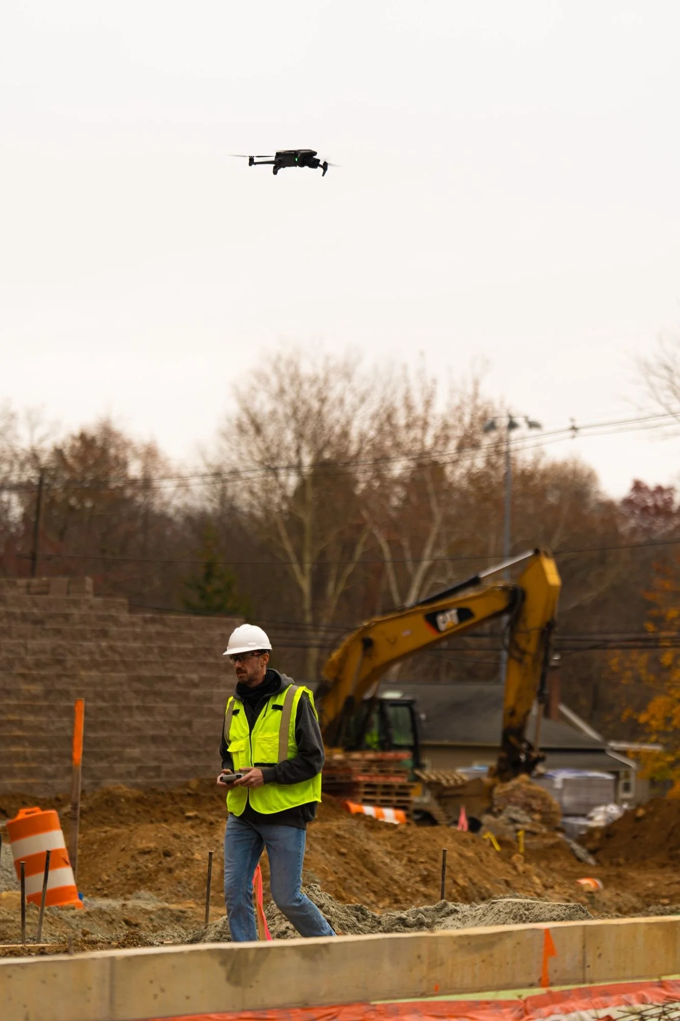 Drone hovering over an excavation site with the pilot watching from the ground
