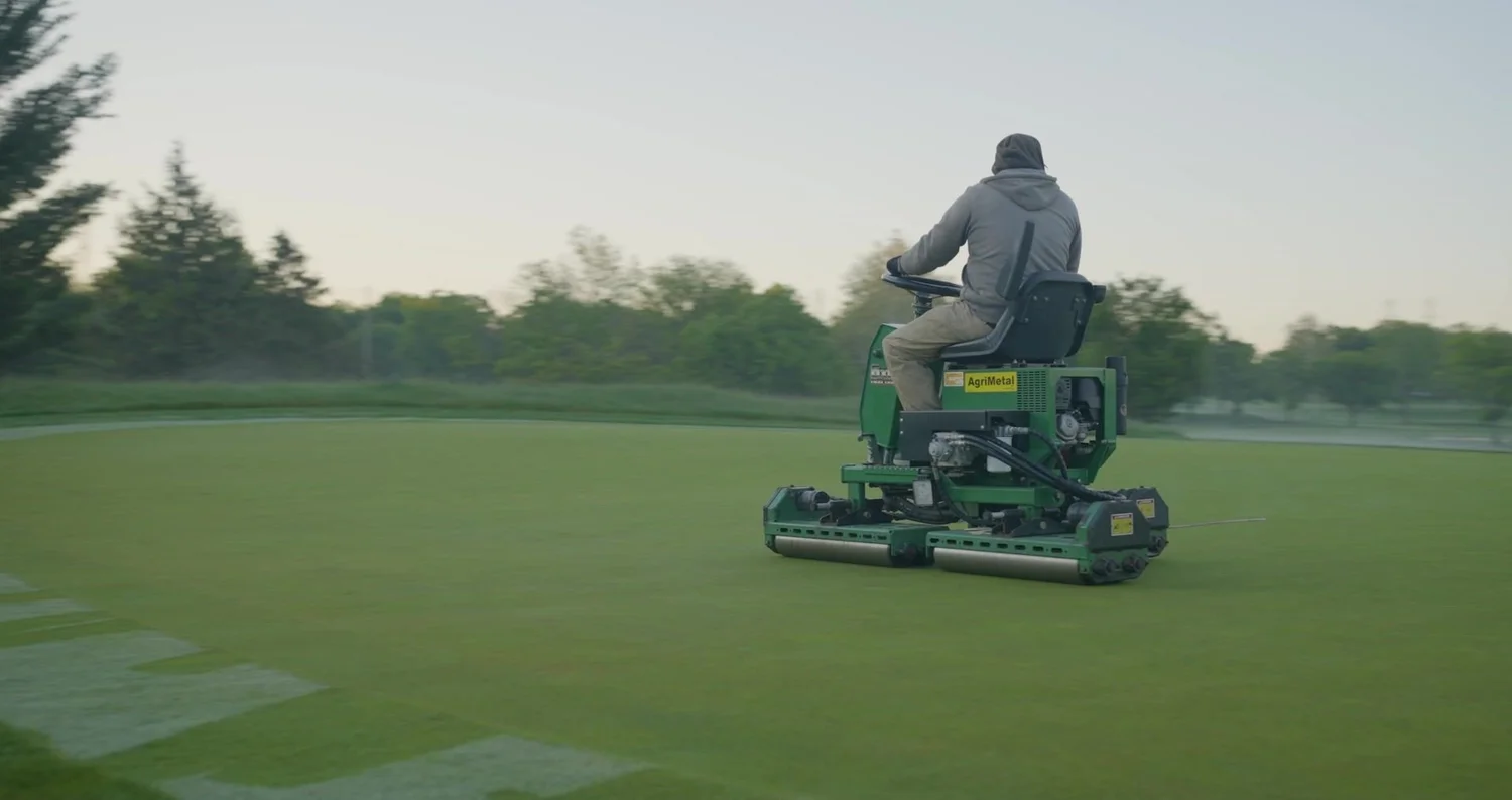 Greenskeeper mowing a golf green at dawn at a private club, soft early light