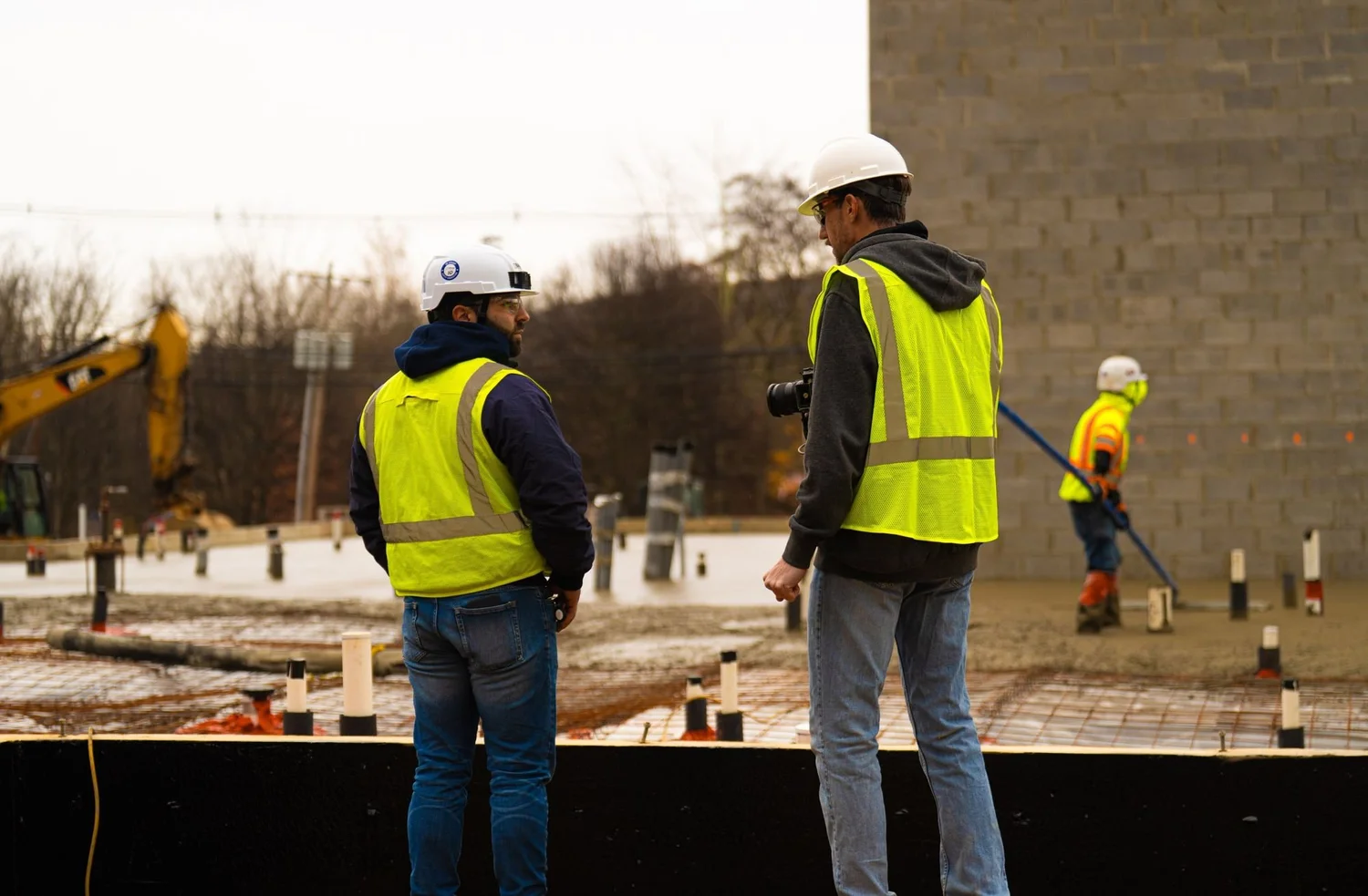 Real estate development video shoot: two crew in hi-vis at a slab edge, one filming