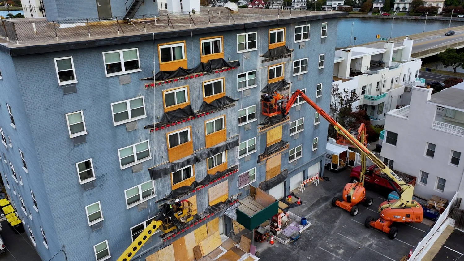 Construction drone video frame of a mid-rise facade renovation with boom lifts and crews