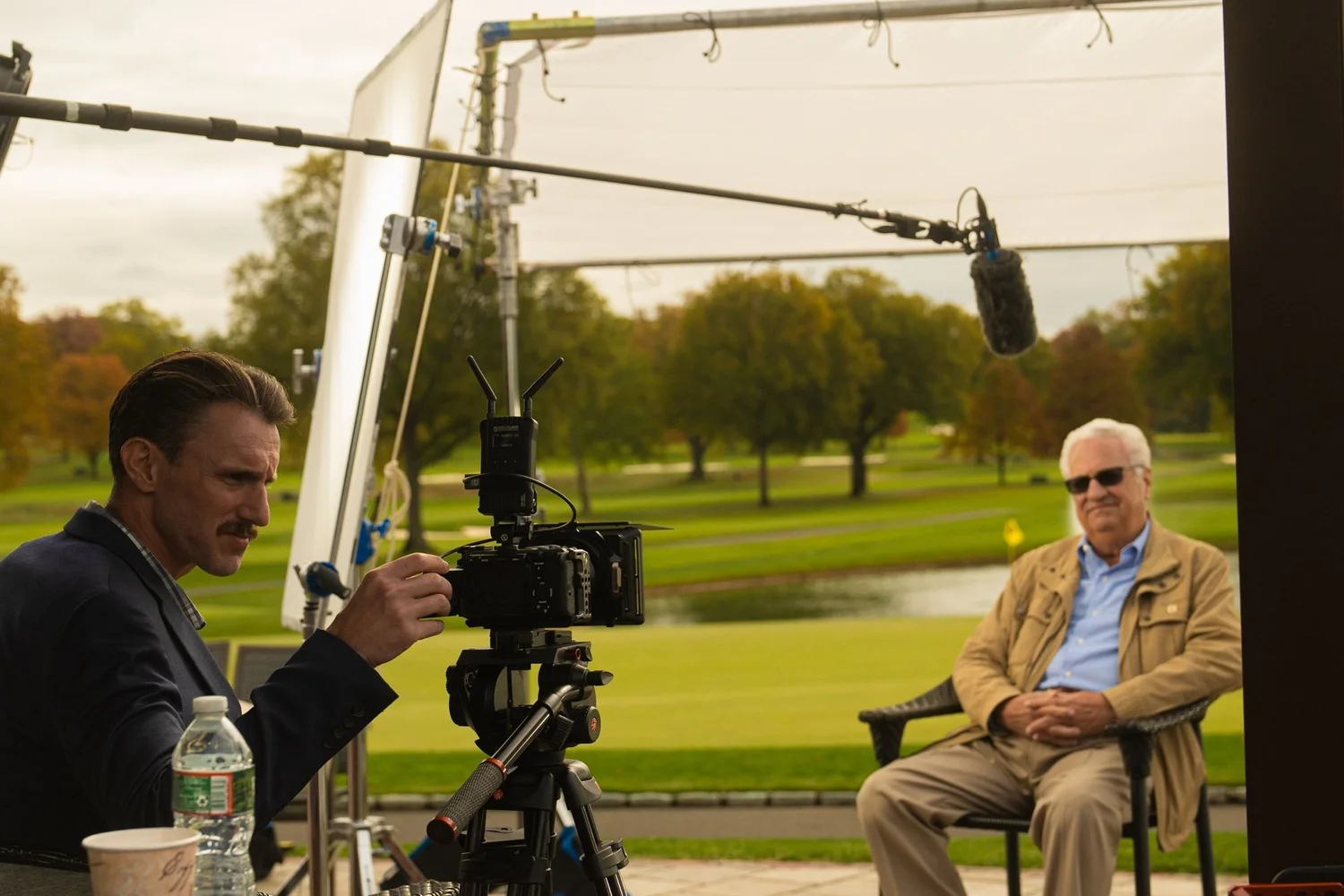 Crew filming at a private club: a member interview under a diffusion frame on the course