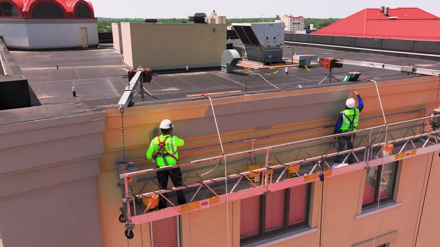 Construction drone video still of two workers on a swing stage restoring a facade