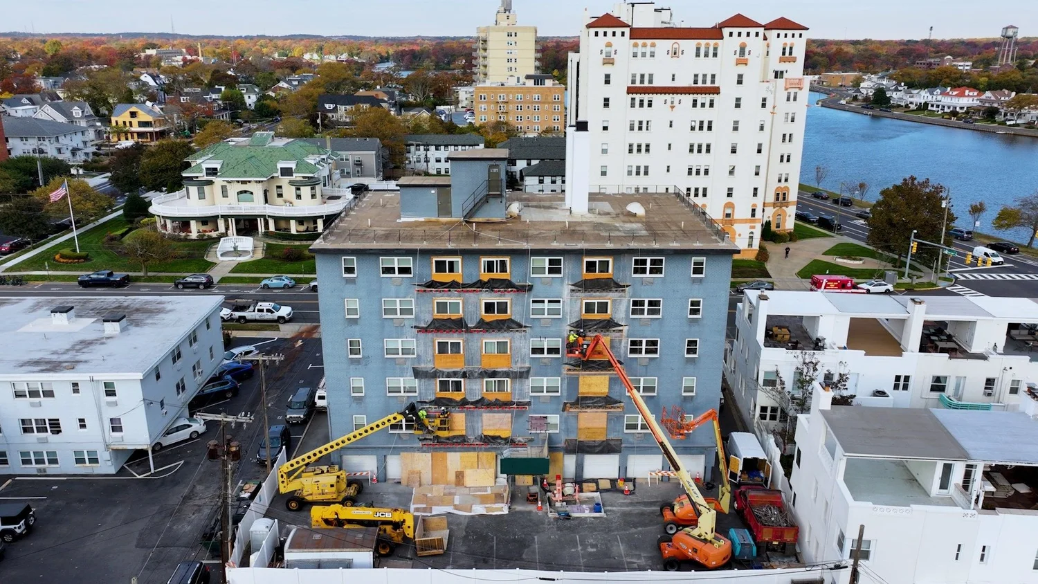Drone aerial of a mid-rise building under exterior renovation with orange boom lifts near the water