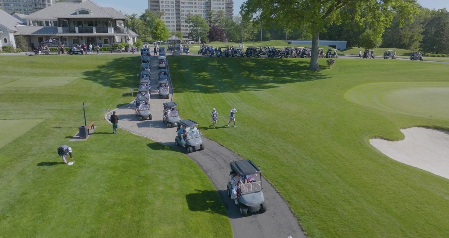 Line of golf carts rolling down the cart path past a private clubhouse