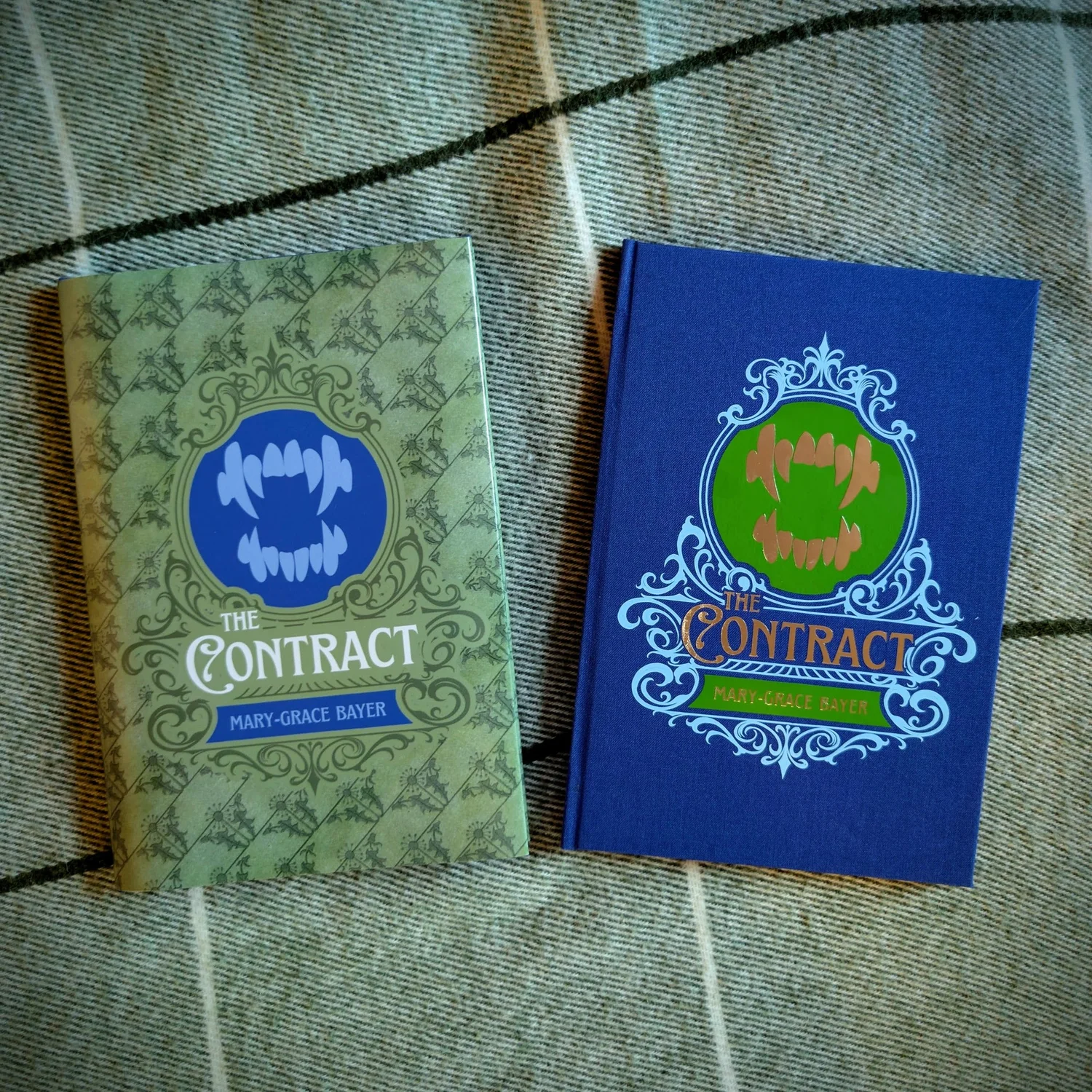 Two copies of The Contract side by side on a wool blanket: the left wears a printed dust jacket, the right shows the blue bookcloth cover with HTV cover art underneath.