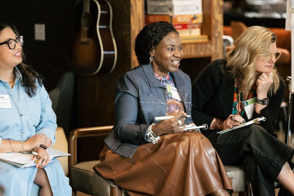 Three women seated in conversation, holding notebooks, at a Henley event