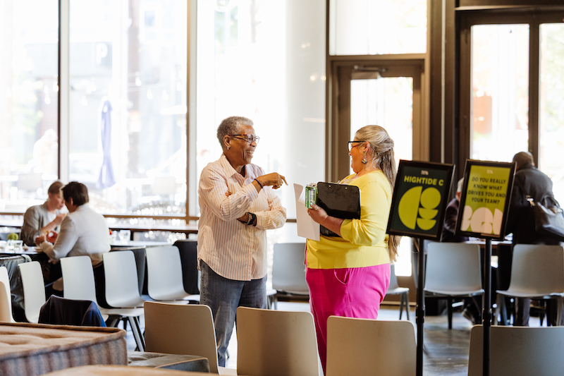 Two women in conversation at a Henley event, one holding a clipboard