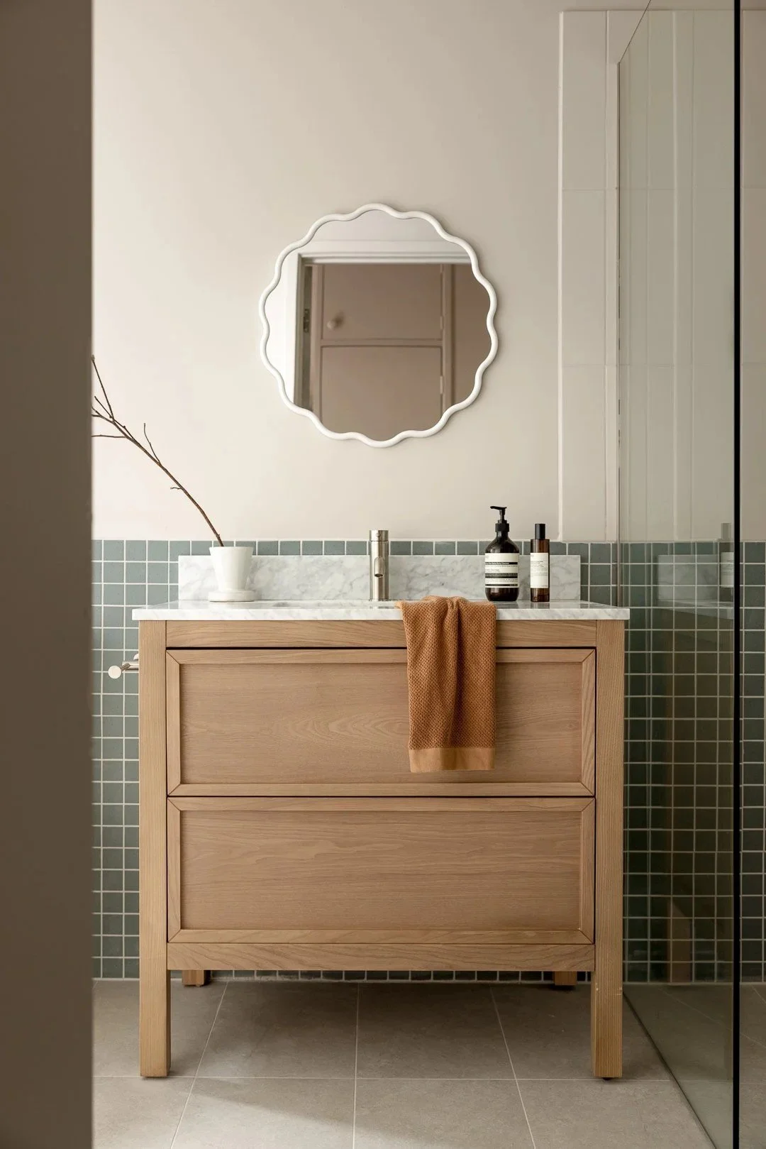 Timber vanity with a scalloped mirror and green tiles