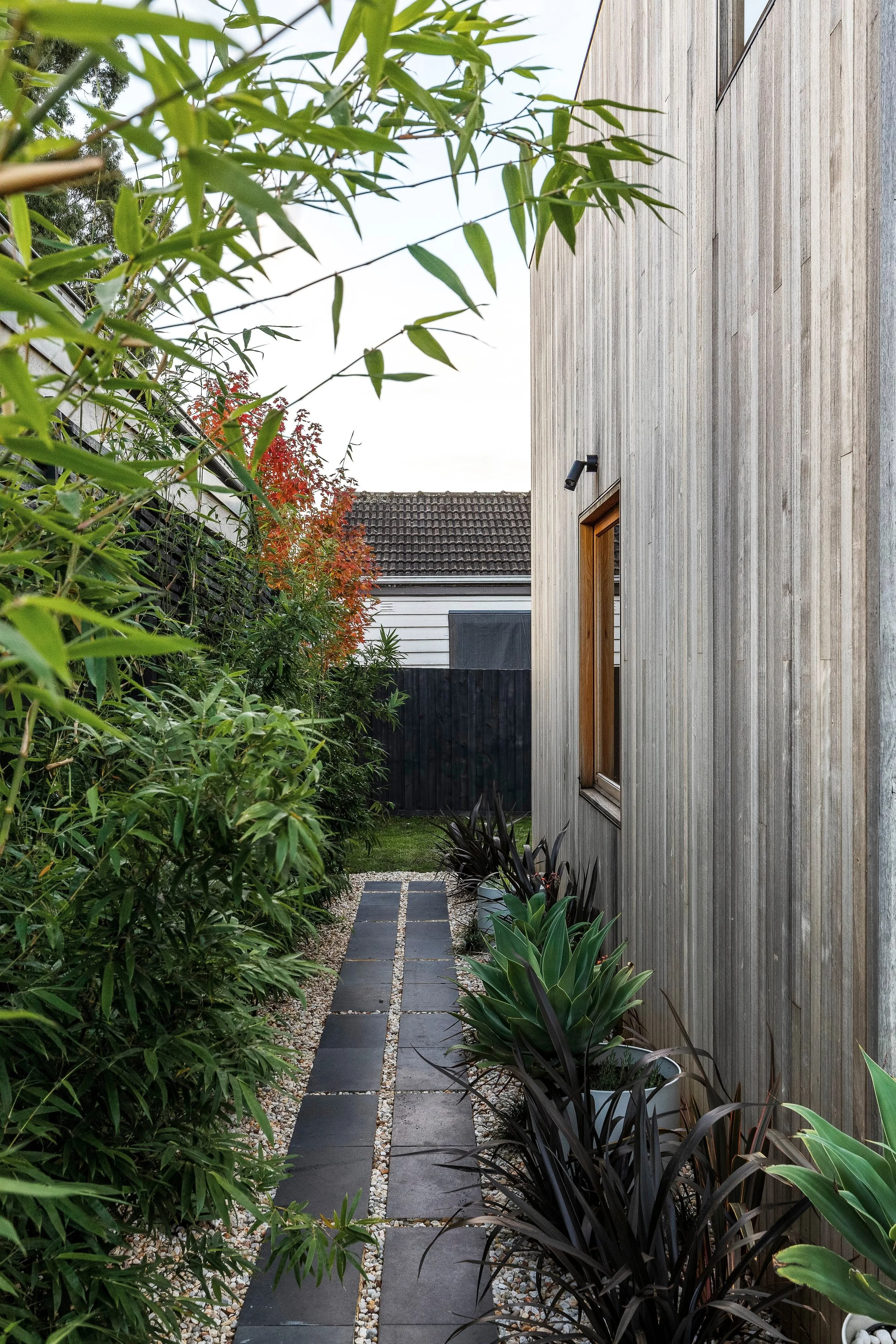 Side path of dark pavers alongside the timber-clad addition and garden beds