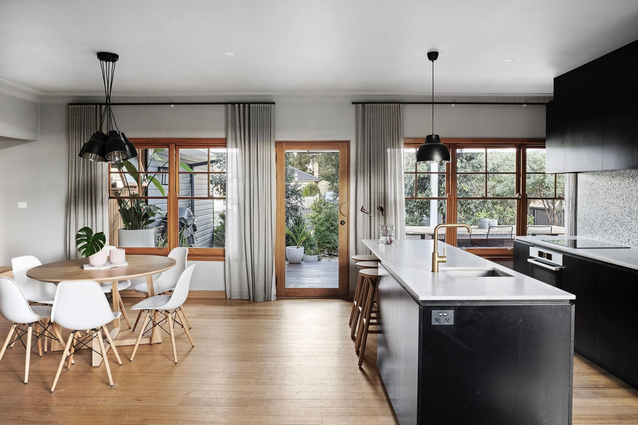 Open-plan dining and kitchen with a round timber table, black pendant, white island and timber floors