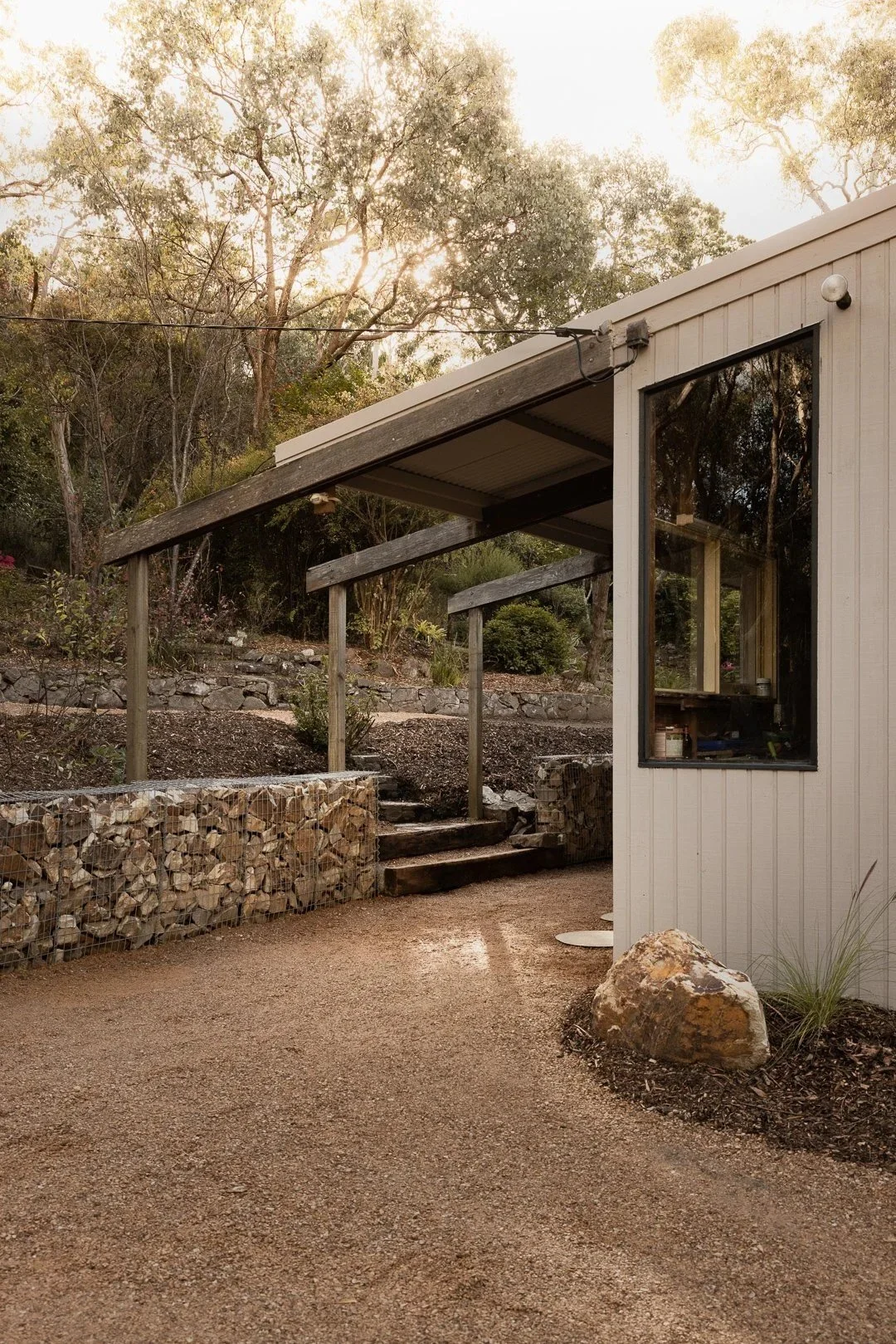 The entry side: a stone retaining wall, steps and the corner of the house with vertical boards