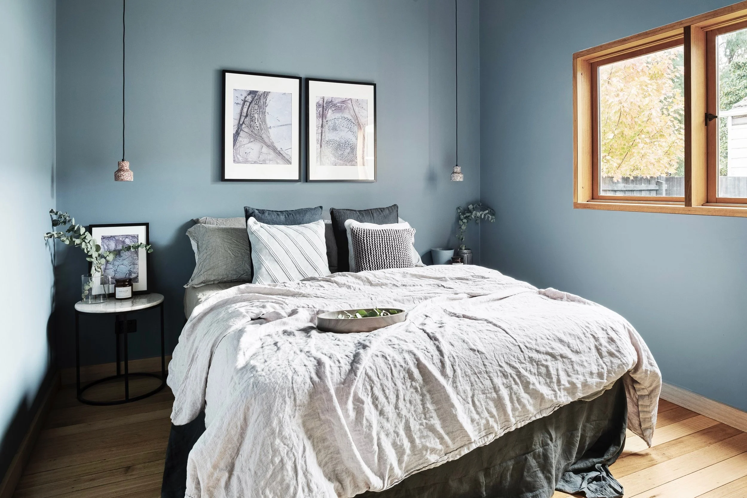 Bedroom painted soft blue with linen bedding and timber-framed windows