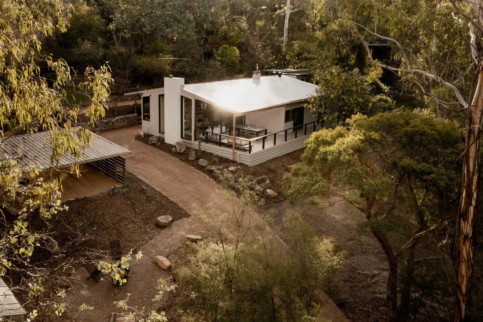 Aerial view of the white house and its covered outdoor room, set into a bush block