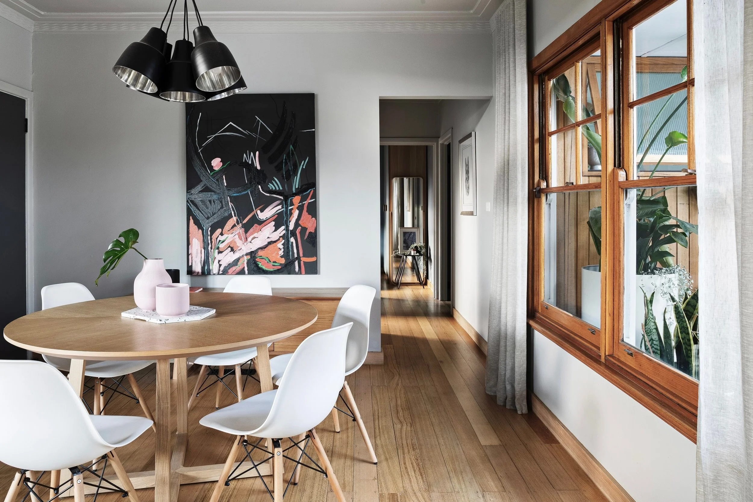 Round timber dining table with white chairs under a black cluster pendant
