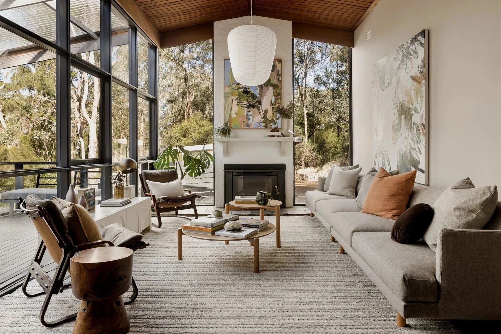 Living room under a timber-lined ceiling, with a wall of glass, a fireplace and a paper pendant